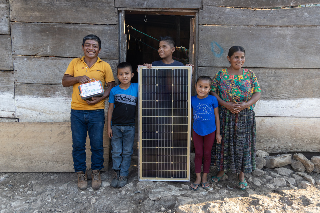 Felipe Tec and his family pose for a photo in the doorway of their home with a solar batter and panel. (Left to right) Felipe Tec, Wilder Edilser Cucul Tec, Nelson Evelio Tec Tiul, Elvia Liliana Cucul Tec, and Angelina Tiul Choc.